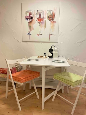 Ein Essbereich mit einem weißen Tisch, zwei Stühlen, einem Gemälde von Weingläsern und einer Kaffeemaschine.