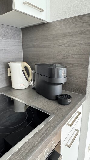 Cuina amb fogó negre, batedora elèctrica blanca i cafetera negra damunt un taulell de fusta.