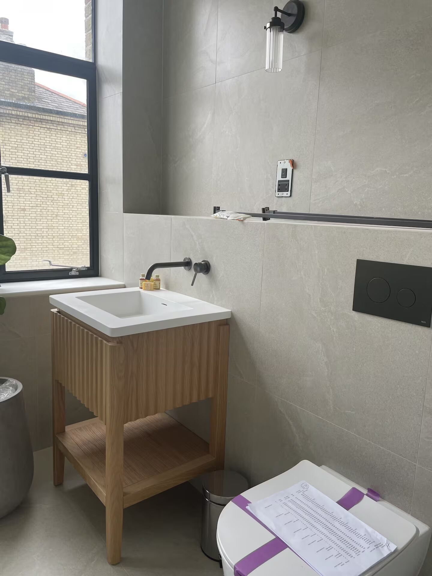 Une salle de bain avec un lavabo blanc, un meuble-lavabo en bois, une fenêtre et un espace douche.