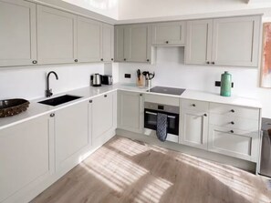 A modern kitchen with white cabinetry, a black sink, and a stainless steel range hood. - Comfortable 2 Bedroom Apartment In Central London (London)
