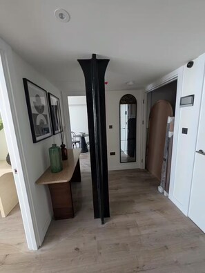 A hallway with a wooden floor, a black pillar, a white door, and a mirror on the wall. - Comfortable 2 Bedroom Apartment In Central London (London)