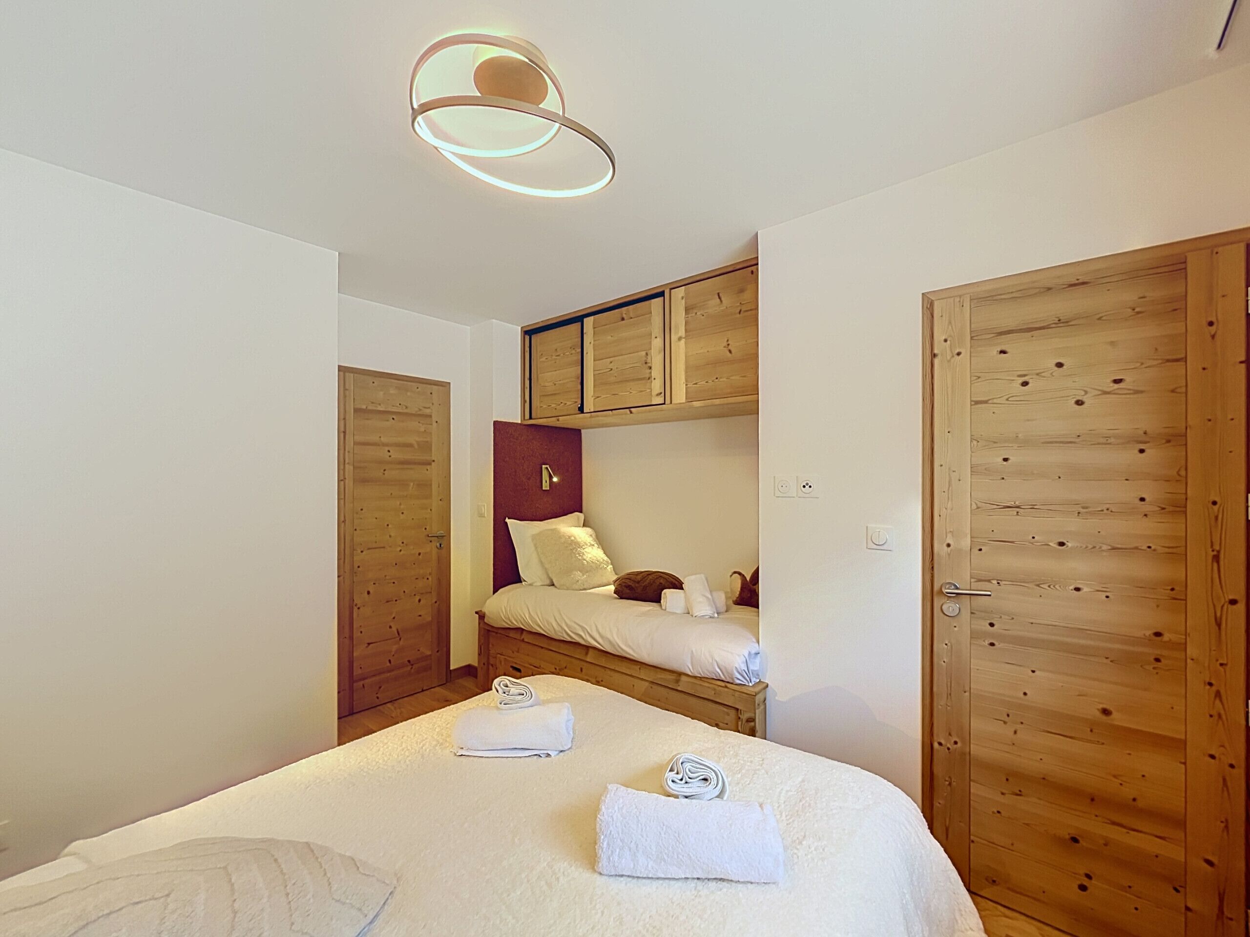 A bedroom with a bed, a wooden wardrobe, and a ceiling light fixture.