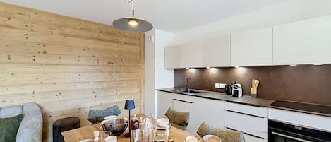 A modern kitchen with white cabinets, a wooden wall, and a dining area with a wooden table set for breakfast.