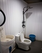 Un baño pequeño con inodoro, lavamanos, ducha y un cubo azul.