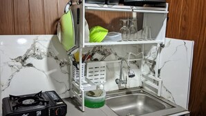 Une cuisine de taille réduite, équipée d’une cuisinière à gaz, d’un évier et d’un égouttoir à vaisselle.