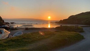 A coastal sunset view with boats docked, a road leading to the beach, and grassy areas. - Dinas Cross Country Park - Holiday Accommodation 20053 (Newport)