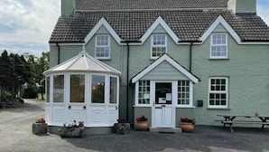 A two-story building with a gabled roof, a small attached structure with a peaked roof, and a paved driveway. - Dinas Cross Country Park - Holiday Accommodation 20053 (Newport)
