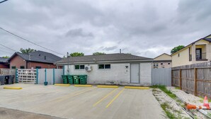 A parking lot with a gated entrance, a building with a grey roof, and a wooden fence. - Dual Houston Homes: 6 Mi to NRG & Med Center (Houston)