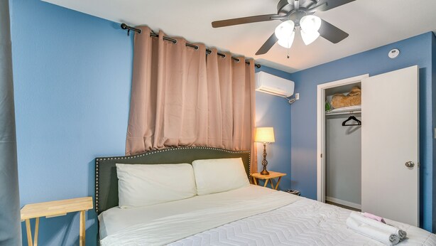 A bedroom with a bed, a ceiling fan, a bedside table, a lamp, and a closet. - Houston Group Stay! 2 Homes Near Museum District (Houston)