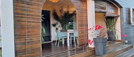 A wooden exterior with a covered porch, a table, chairs, and potted plants.