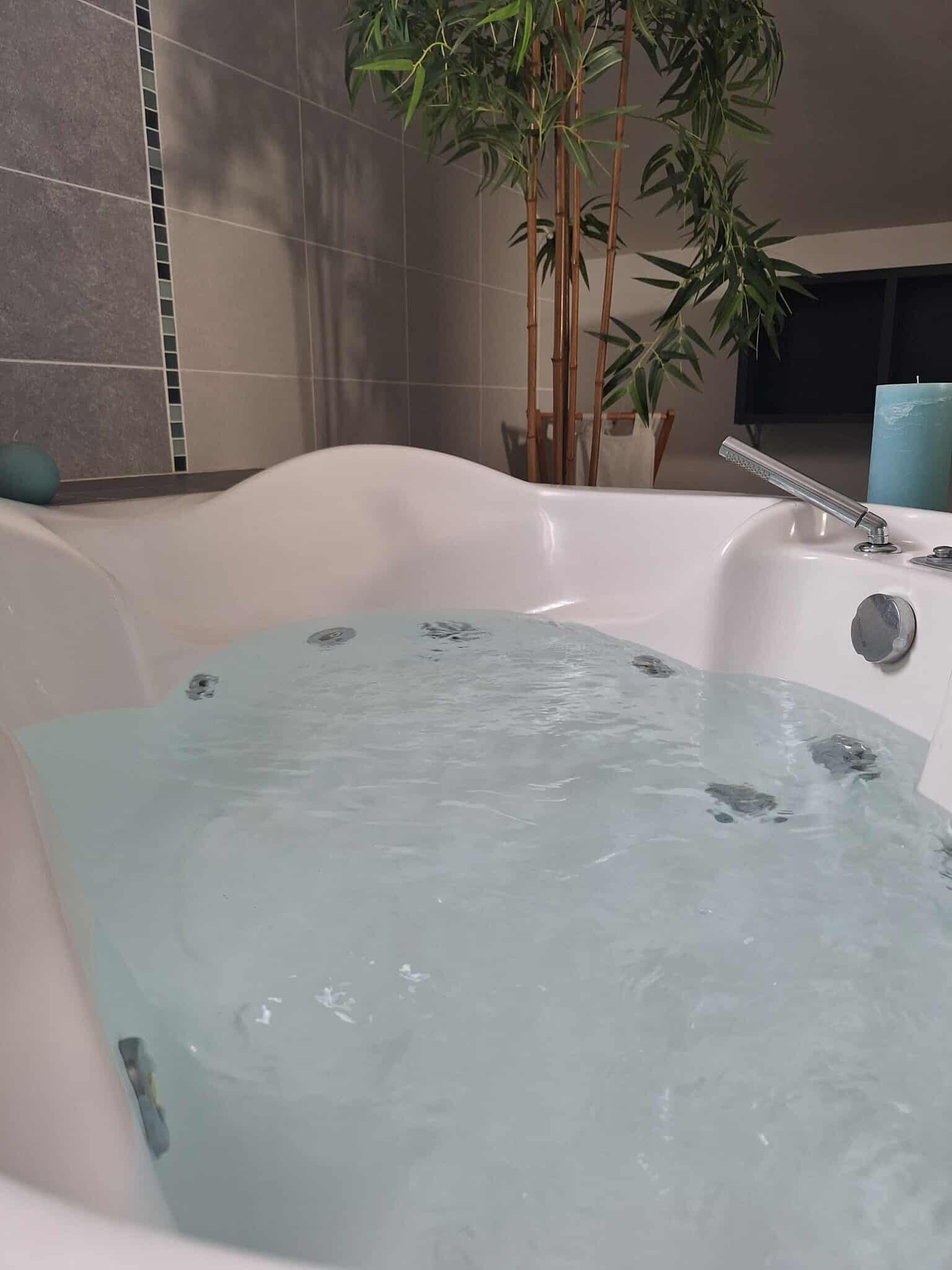 A bathtub filled with water, a bamboo plant, and a blue towel.