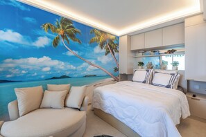 A bedroom with a beach mural, a bed, a sofa, and a nightstand with decorative items. - 180° ocean view, 20 m² terrace, beach right below the residence, private parking, Monaco (Roquebrune-Cap-Martin)