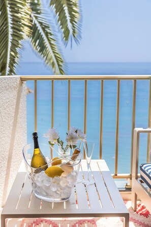 Ein Tisch mit einer Flasche, Gläsern, Blumen und Eiswürfeln auf einem Balkon mit Meerblick.