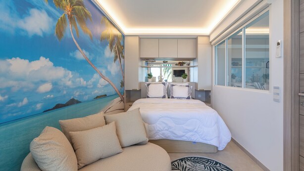 Een slaapkamer met een bed, een sofa, een keukenhoek en een groot muurdecoratie van een strandgezicht.