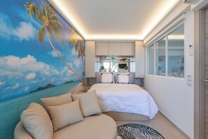 Un dormitorio con cama, sofá, zona de cocina y un gran mural con escena de playa.