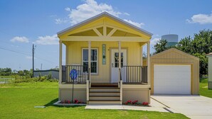 Una piccola casa gialla con un portico, un garage e una torre d'acqua sullo sfondo.