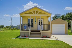 A small yellow house with a porch, a garage, and a water tower in the background. - Tiny Home Retreat Close to Lake Granbury (Granbury)