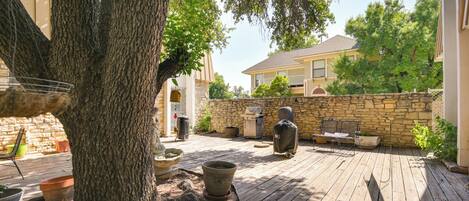 A wooden deck with outdoor furniture, a stone wall, and a large tree.