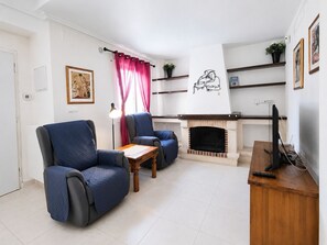 Ein Wohnzimmer mit zwei Sesseln, einem kleinen Tisch, einem Kamin und einem Fernseher auf einem Holzgestell.
