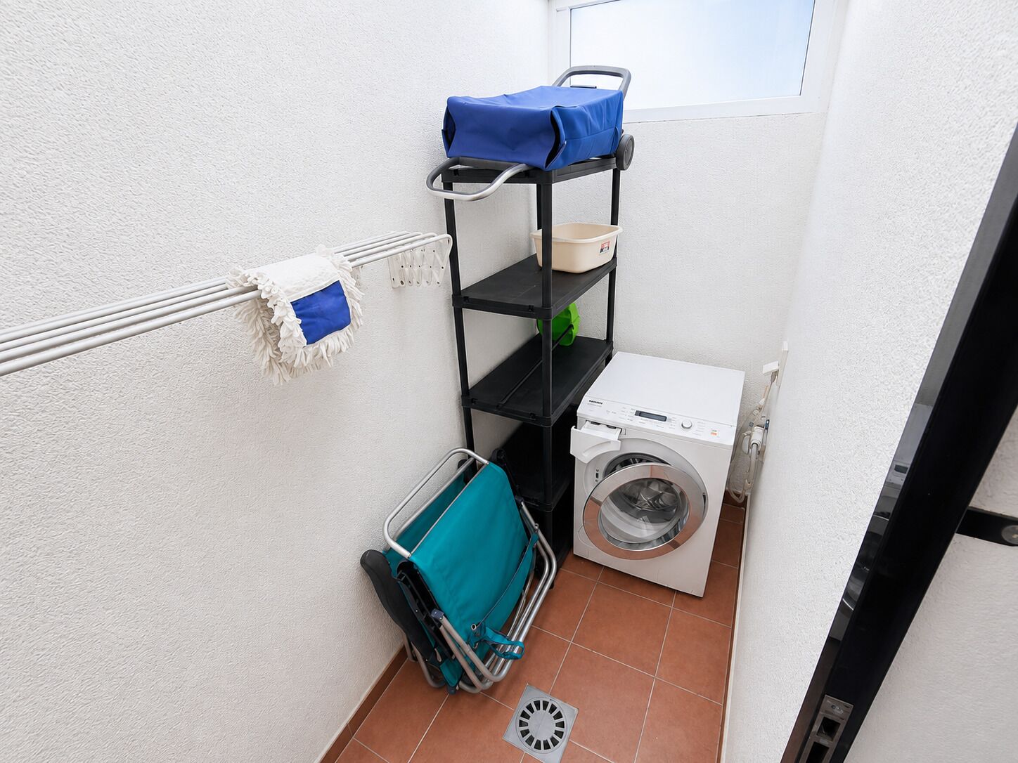 A laundry area with a washing machine, a drying rack, and a shelf with cleaning supplies.