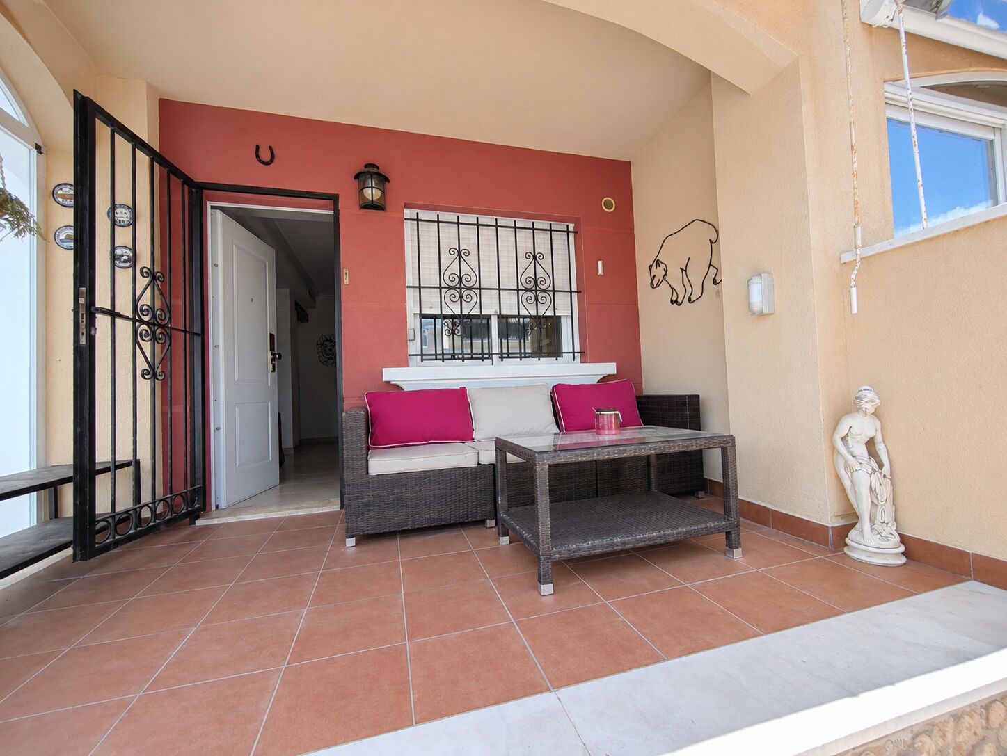 Un espace patio aménagé avec un canapé en osier, une table et une statue.