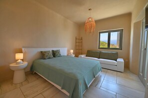 Une chambre à coucher avec un lit, des tables de chevet, une lampe, un canapé et une fenêtre donnant sur un beau paysage.