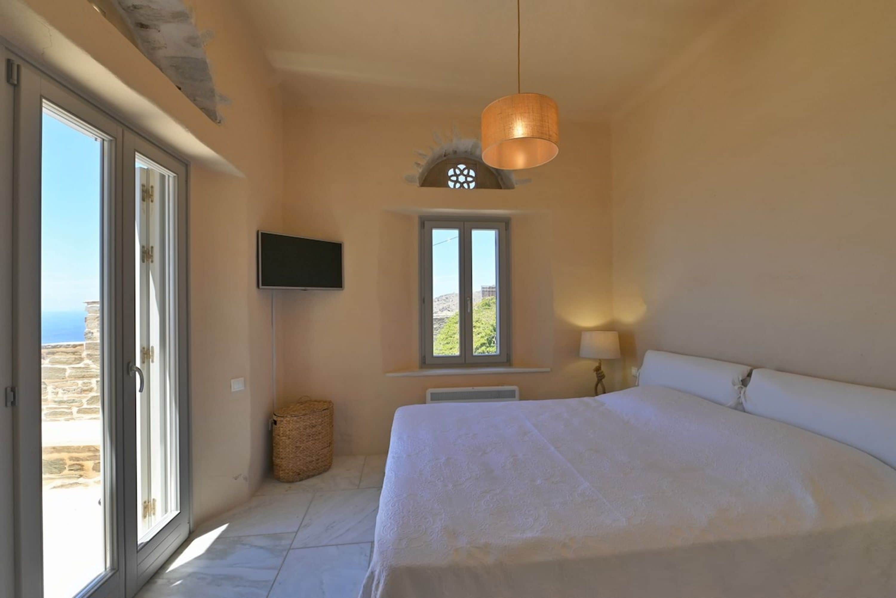 A bedroom with a large bed, a television, a window with a view, and a ceiling light fixture.