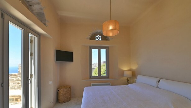 Un dormitorio con una cama grande, televisor, ventana con vistas y una lámpara en el techo.