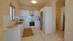 Una cocina compacta con muebles blancos, horno empotrado, refrigerador y ventana.