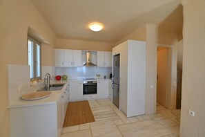 Eine kompakte Küche mit weißen Schränken, einem eingebauten Backofen, einem Kühlschrank und einem Fenster.