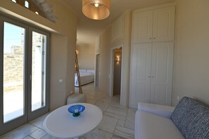 Ein geräumiger Raum mit einem großen Schiebeglasfenster, das auf einen Balkon führt, ein weißes Sofa, ein runder Tisch mit einem blauen Gegenstand und ein Kleiderschrank.