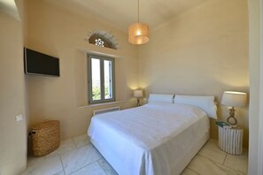 A bedroom with a bed, a television on the wall, a window, and a lamp. - Dioni Tinos sea View Elegant Villa (Tinos)