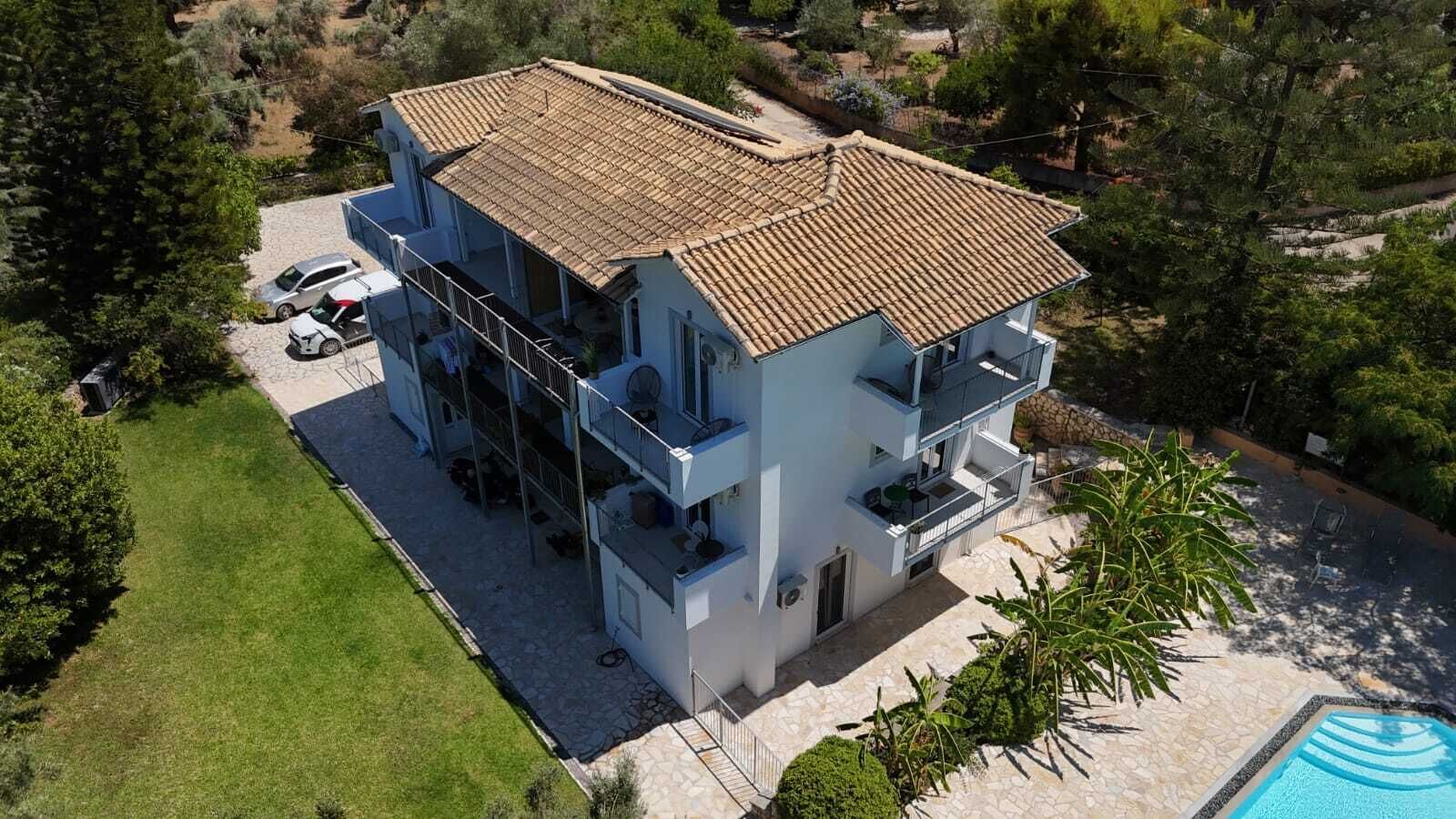 A multi-story building with a tiled roof, a swimming pool, and a well-maintained lawn.