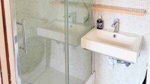 Un baño moderno con ducha de vidrio, un lavamanos blanco con dispensador de jabón y un espejo sobre el lavamanos.