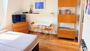 Un dormitorio con una cama, un escritorio, un televisor, una lámpara y una estantería.