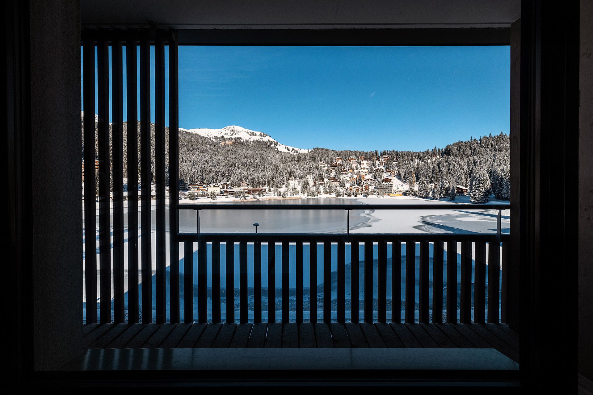 Vista da un balcone con ringhiera su un paesaggio innevato con un lago e edifici.