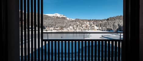A view from a balcony with a railing, overlooking a snow-covered landscape with a lake and buildings.
