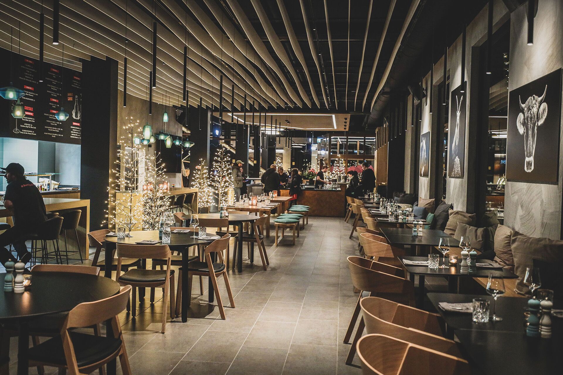 An indoor dining area with multiple tables and chairs, a bar counter, and decorative lighting.