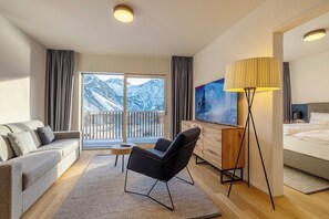 A hotel room with a balcony, a sofa, a chair, a TV, a lamp, and a bed.