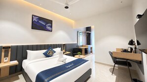 A modern hotel room with a bed, bedside tables, a desk, a chair, a ceiling fan, and a wall-mounted TV. - Hotel Kyzen - Shamshabad Airport (Hyderabad)
