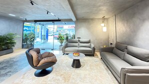 A modern lobby with a sofa, armchair, and coffee table, a glass door entrance, and potted plants. - Hotel Kyzen - Shamshabad Airport (Hyderabad)