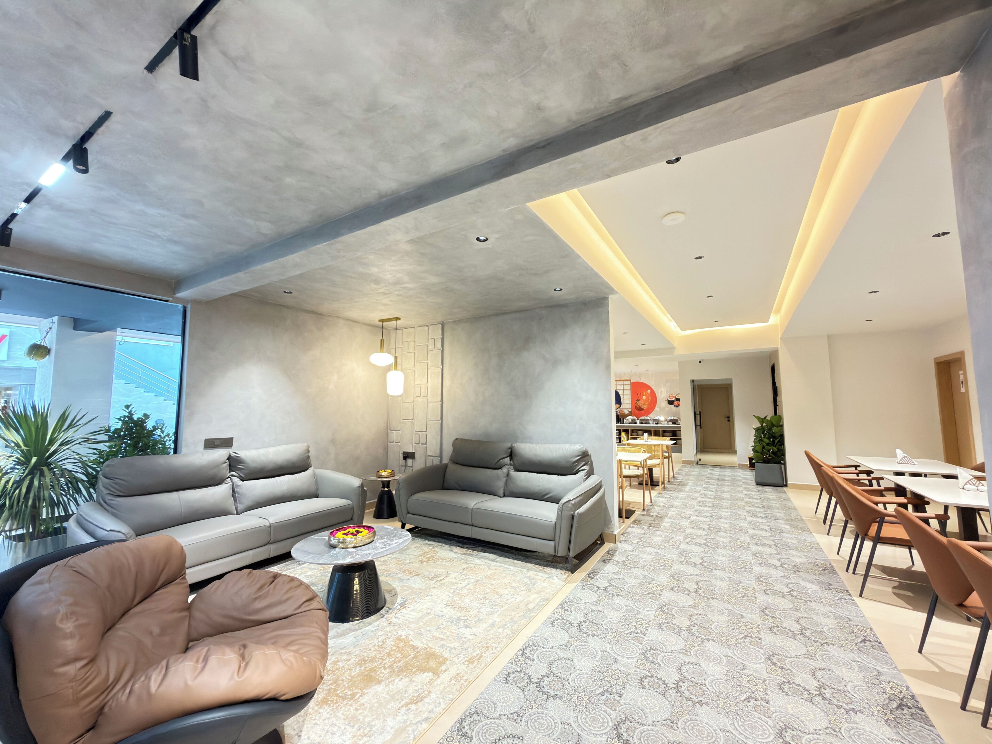 Una sala de estar moderna con un sofá gris, un sillón marrón y un comedor con una mesa y sillas.