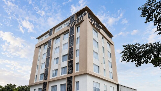 A multi-story hotel with a modern design, featuring a prominent entrance with a blue sign, and a parking area in front. - Hotel Kyzen - Shamshabad Airport (Hyderabad)
