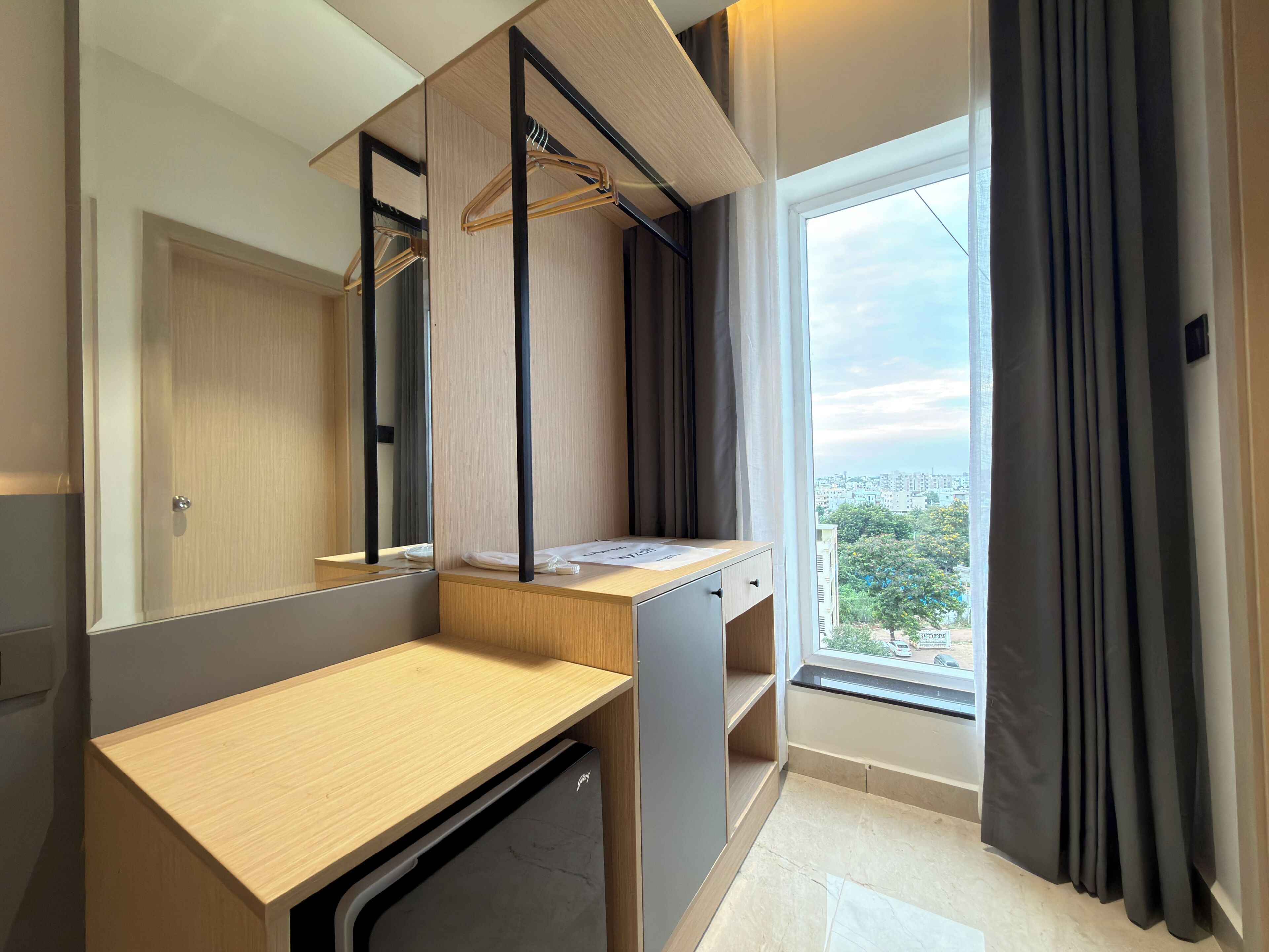 Un baño moderno con tocador de madera, espejo, toallero y ventana con cortinas.