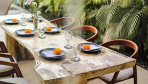 Mesa de madeira rústica posta com pratos, copos e um vaso com flores.