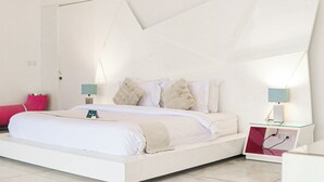 Een moderne hotelkamer met een wit bed, twee bedlampen, een nachtkastje en een rood sierkussen.