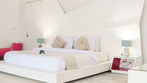 A modern hotel room with a white bed, two bedside lamps, a bedside table, and a red accent pillow. - Calma Cliff Villas  (Ungasan)