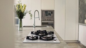 A modern kitchen with a gas stove, a stainless steel sink, and a vase with flowers. - Calma Cliff Villas  (Ungasan)