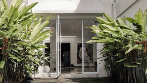 A modern building entrance with a glass door, surrounded by large green plants. - Calma Cliff Villas  (Ungasan)