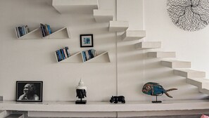 Uma escadaria com estantes de livros em ambos os lados, um quadro emoldurado e objetos decorativos.